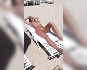 Hete vrouw met mooi lichaam en geschoren kutje is aan het zonnebaden op het strand